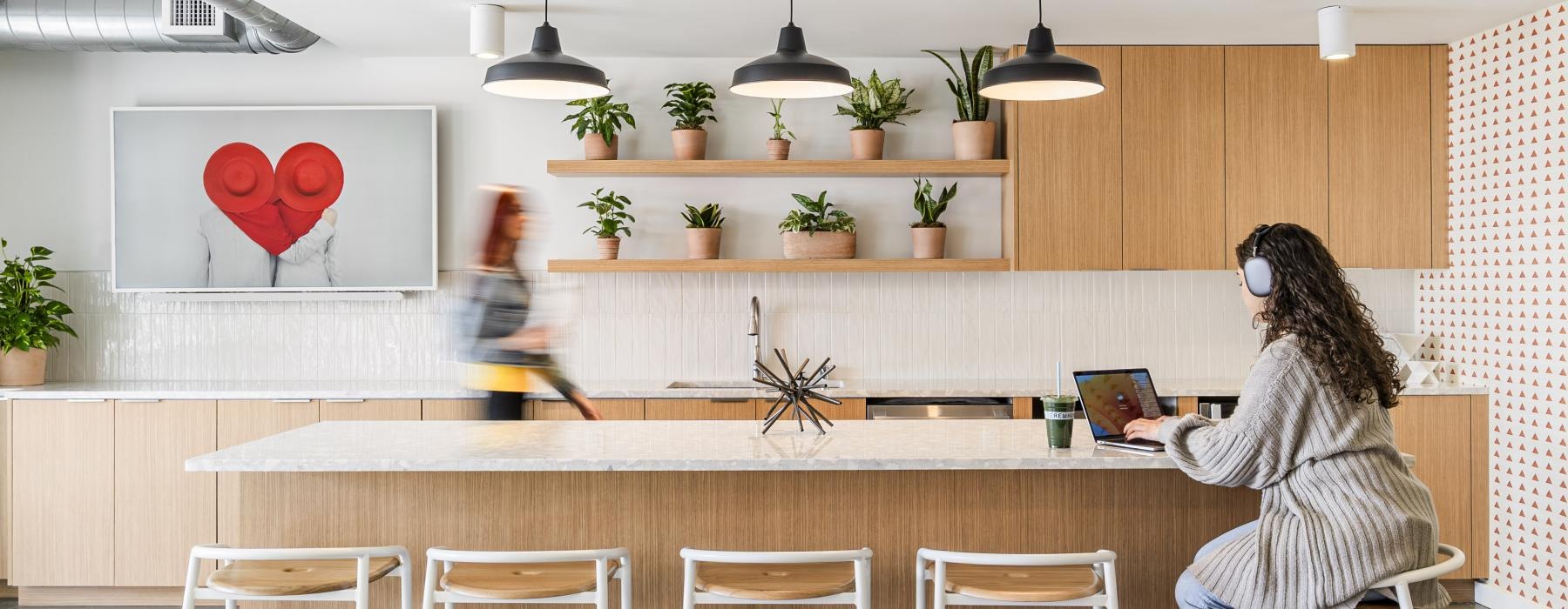 a person sitting at a table with a laptop and a person standing behind the counter